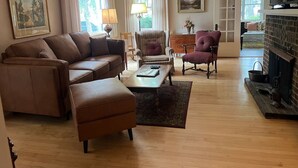 Ein geräumiges Wohnzimmer mit einem braunen Ledersofa, einem Couchtisch und zwei Sesseln. Im Hintergrund ist ein Kamin zu sehen.