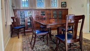 Ein Esszimmer mit Holztisch und -stühlen, einem gemusterten Teppich und einer Vitrine mit Glastüren.