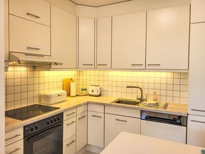 Een koelkast, een oven, een vaatwasser, kookgerei, borden en bestek