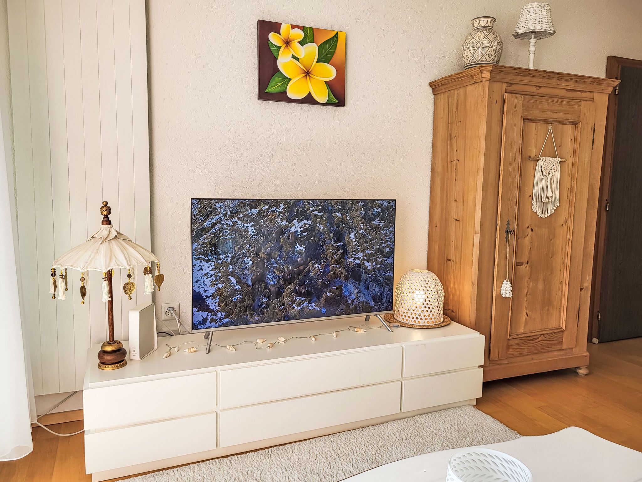Un salon avec un téléviseur à écran plat posé sur une console blanche, un meuble en bois, une lampe décorative et un tableau accroché au mur.