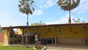 A yellow building with a patio area, a brick oven, and palm trees. - Pousada Sítio Boas Novas  (Caucaia)