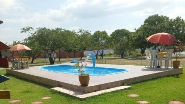A swimming pool with a water feature, surrounded by a well-maintained lawn and outdoor furniture. - Pousada Sítio Boas Novas  (Caucaia)