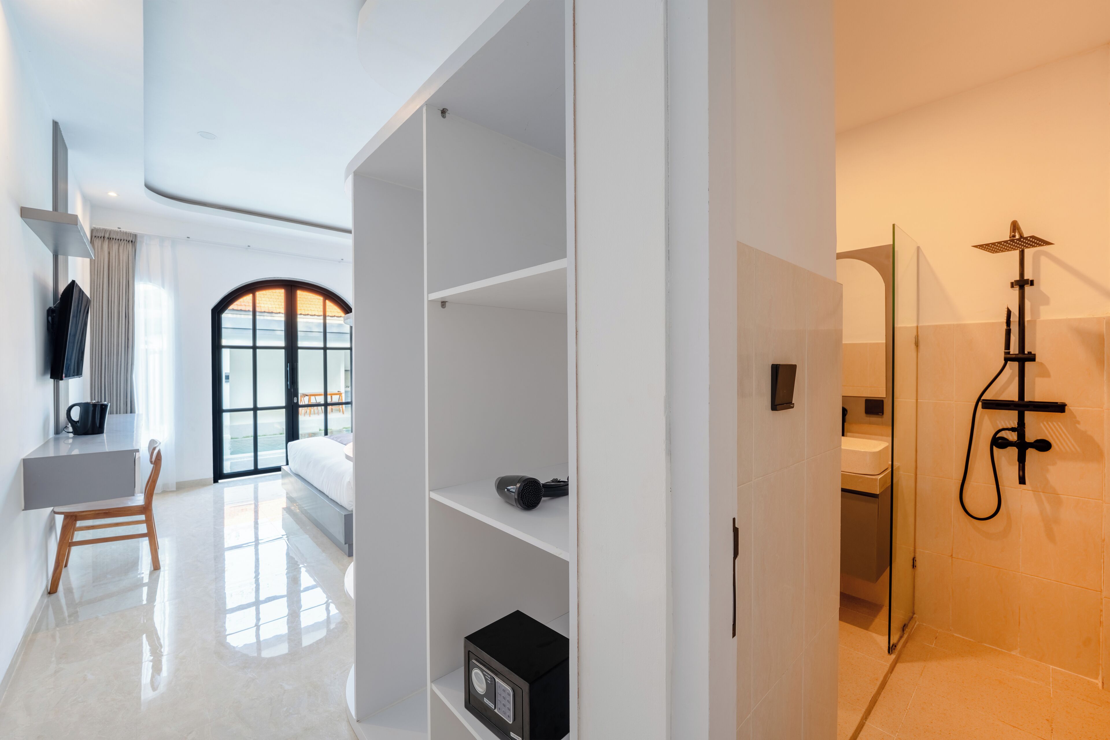 Una habitación de hotel moderna con un ventanal grande, un escritorio, una silla, un armario y zona de ducha.