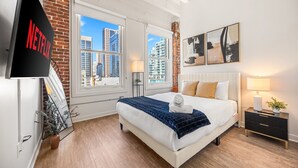 A modern bedroom with a large bed, a TV, and a view of the city. - Cityscape Luxe - Walk to Gaslamp & Petco (San Diego)