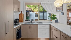 Ett modernt kök med träskåp, en inbyggd ugn, en diskho och ett fönster med utsikt över ett hus och grönområden.