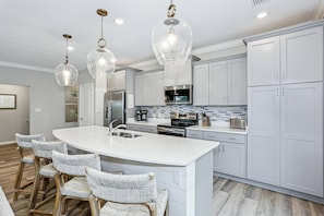 A modern kitchen with white cabinets, a central island, and hanging pendant lights.