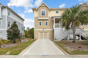 A residential building with a paved driveway, a palm tree, and a staircase leading to a balcony.