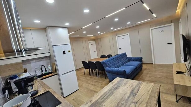 A modern kitchen with a built-in stove, a dining area with a blue sofa, and a wooden table. - Central Guest house (Ulaanbaatar)