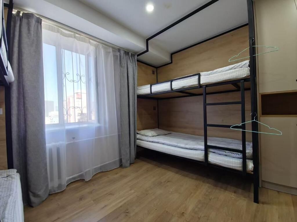 A bunk bed room with a window and curtains, wooden flooring, and a wardrobe.