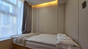 A small, single-bed room with a window, a bedside table, and a wall-mounted light. - Central Guest house (Ulaanbaatar)