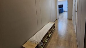 A hallway with a bench and shoe storage, leading to a room with a TV and a desk. - Central Guest house (Ulaanbaatar)