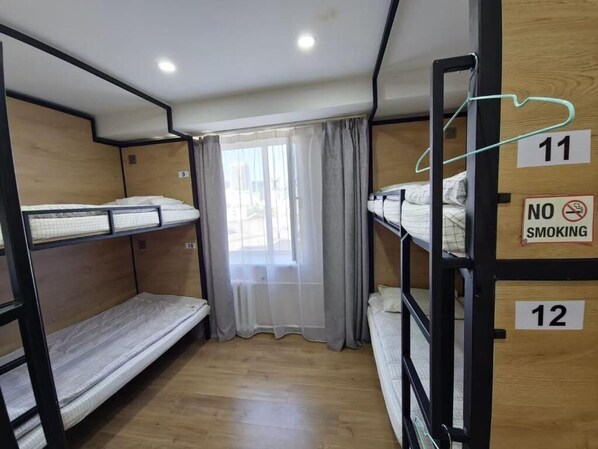 Habitación tipo dormitorio con literas, una ventana con cortinas y un cartel de 'No Fumar'.