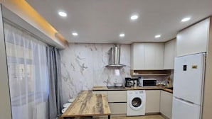 A compact kitchen with a wooden table, a washing machine, a microwave, and a refrigerator. - Central Guest house (Ulaanbaatar)