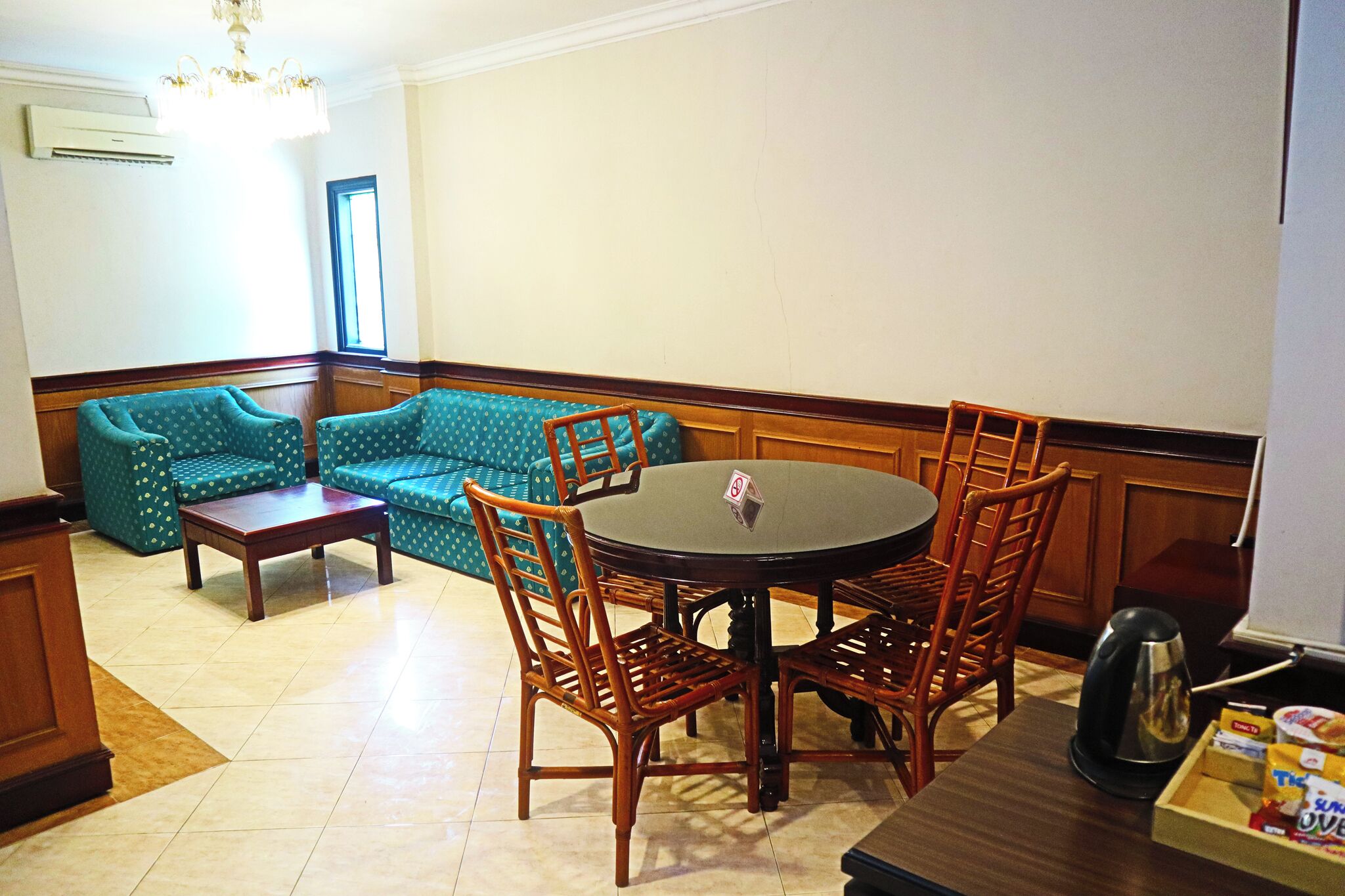 A dining area with a round table, wooden chairs, a sofa, and a coffee maker.