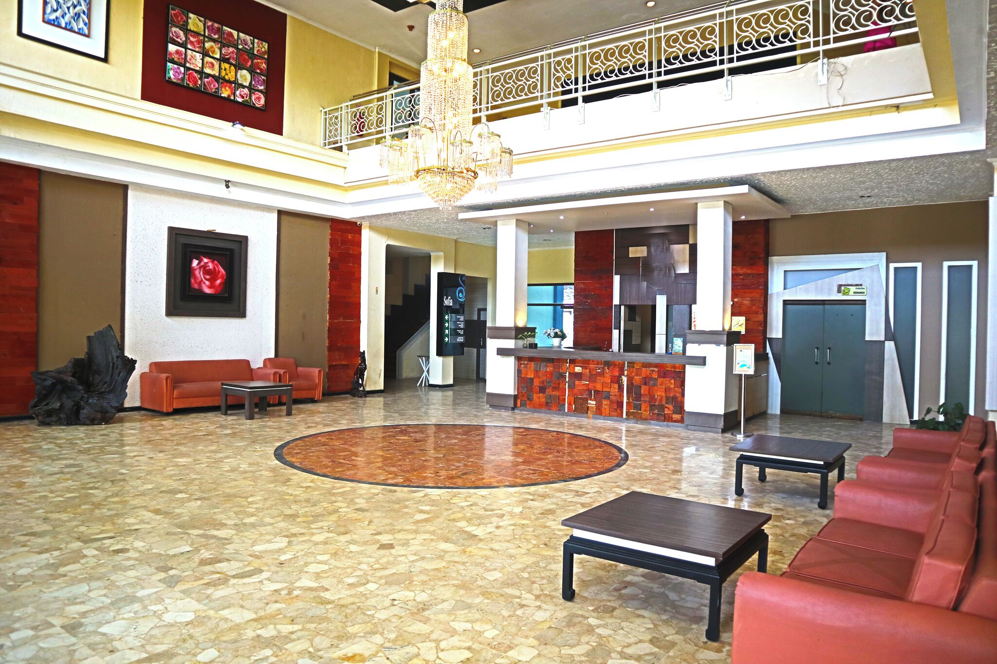 Un hall d’entrée spacieux avec un plafond haut, un lustre central, un comptoir de réception et un espace détente avec des canapés et une table basse.