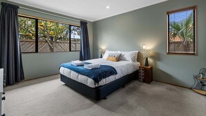 A bedroom with a large bed, a nightstand, a lamp, and a window with curtains. - Hideaway on Edgecumbe (Tauranga)