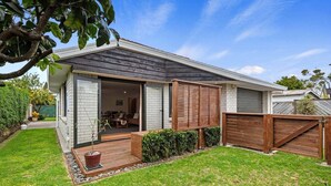 A modern house with a covered patio, a wooden fence, and a well-maintained lawn. - Hideaway on Edgecumbe (Tauranga)