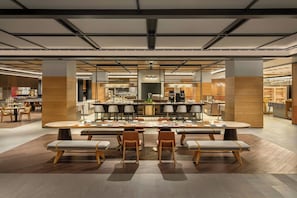Un restaurante moderno con una barra central, varias áreas de estar y vistas a la cocina.