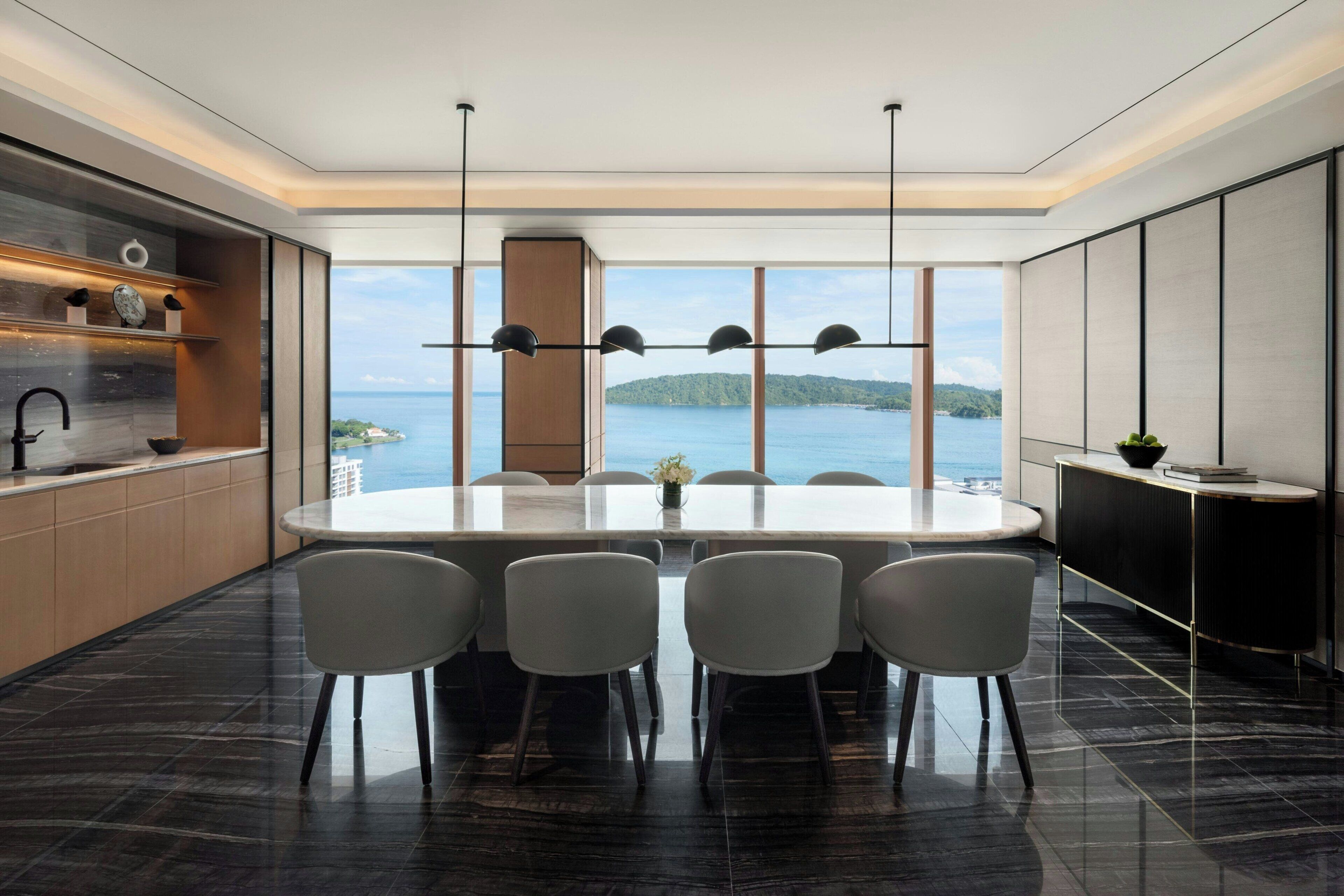 A modern kitchen with a large island, a dining area with a round table and chairs, and a view of the sea.