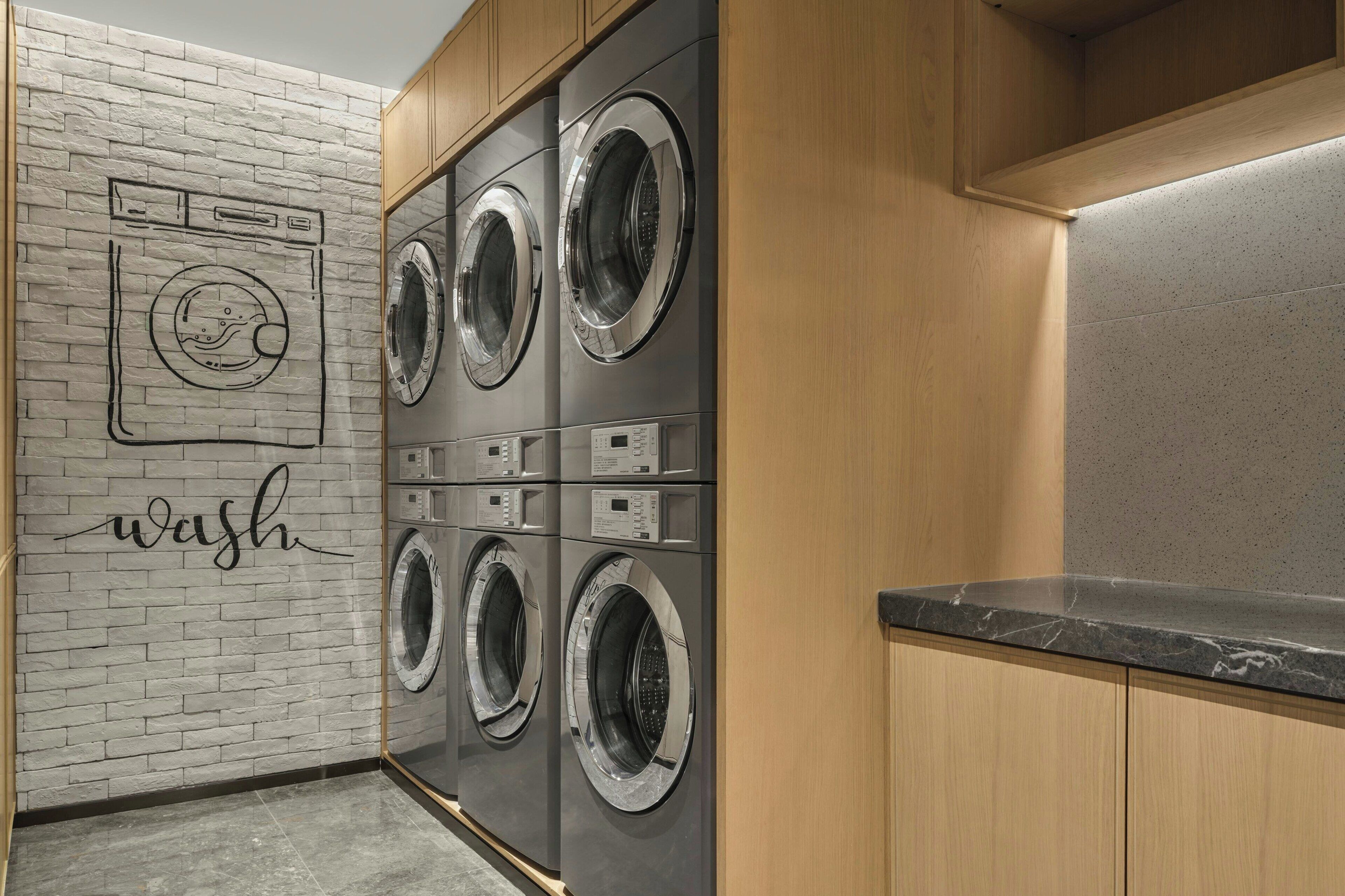 A laundry area with four front-loading washing machines, a wall-mounted dryer, and a wooden cabinet.