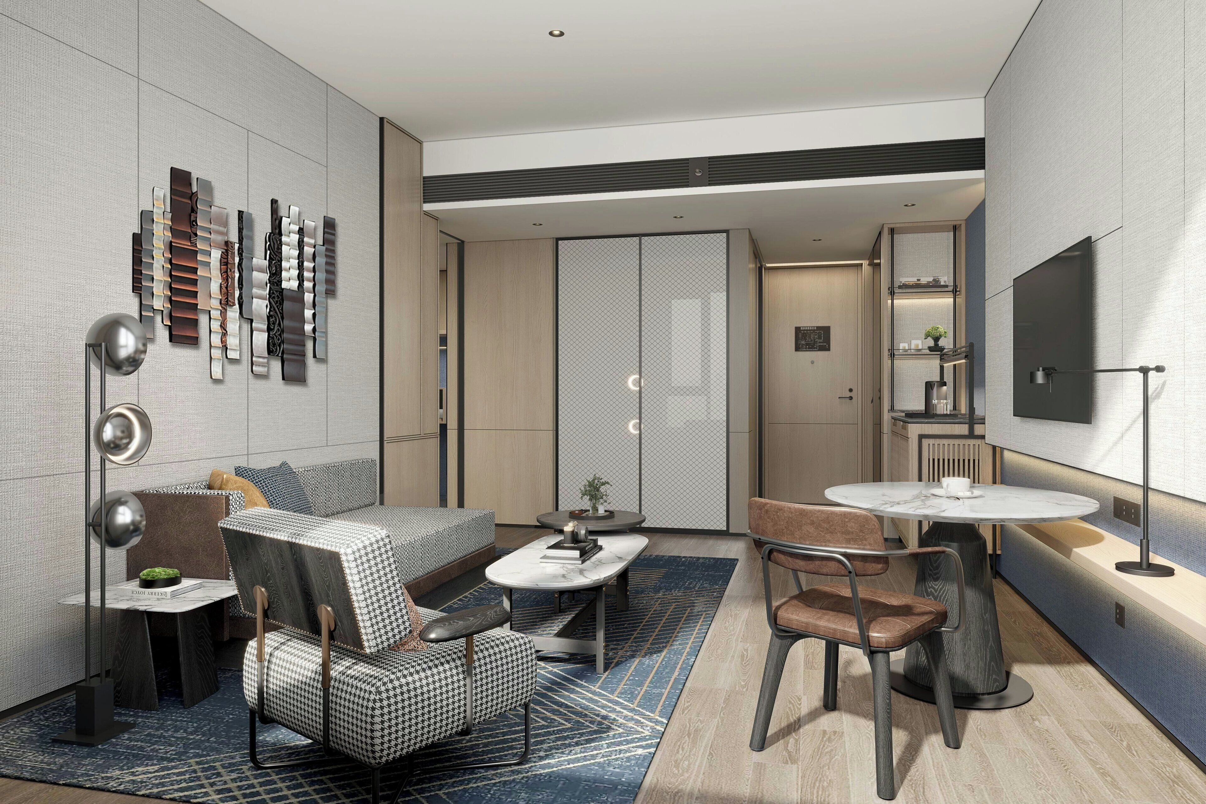 A modern hotel room with a sofa, a dining table, a chair, a small side table, and a decorative wall piece.