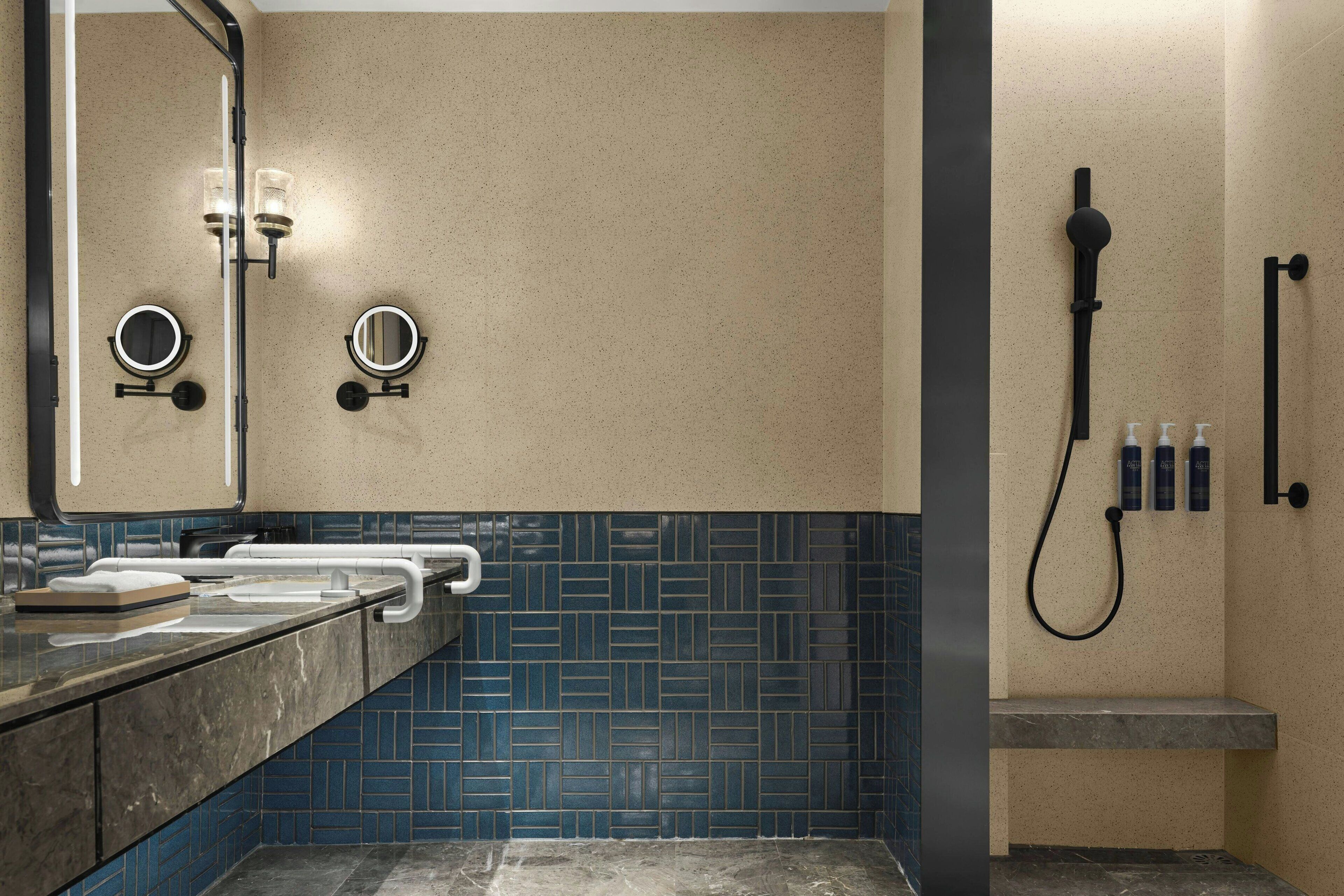 Un baño moderno con encimera de mármol, dos espejos redondos, un perchero, zona de ducha con cabezal de ducha manual y dispensador de jabón.