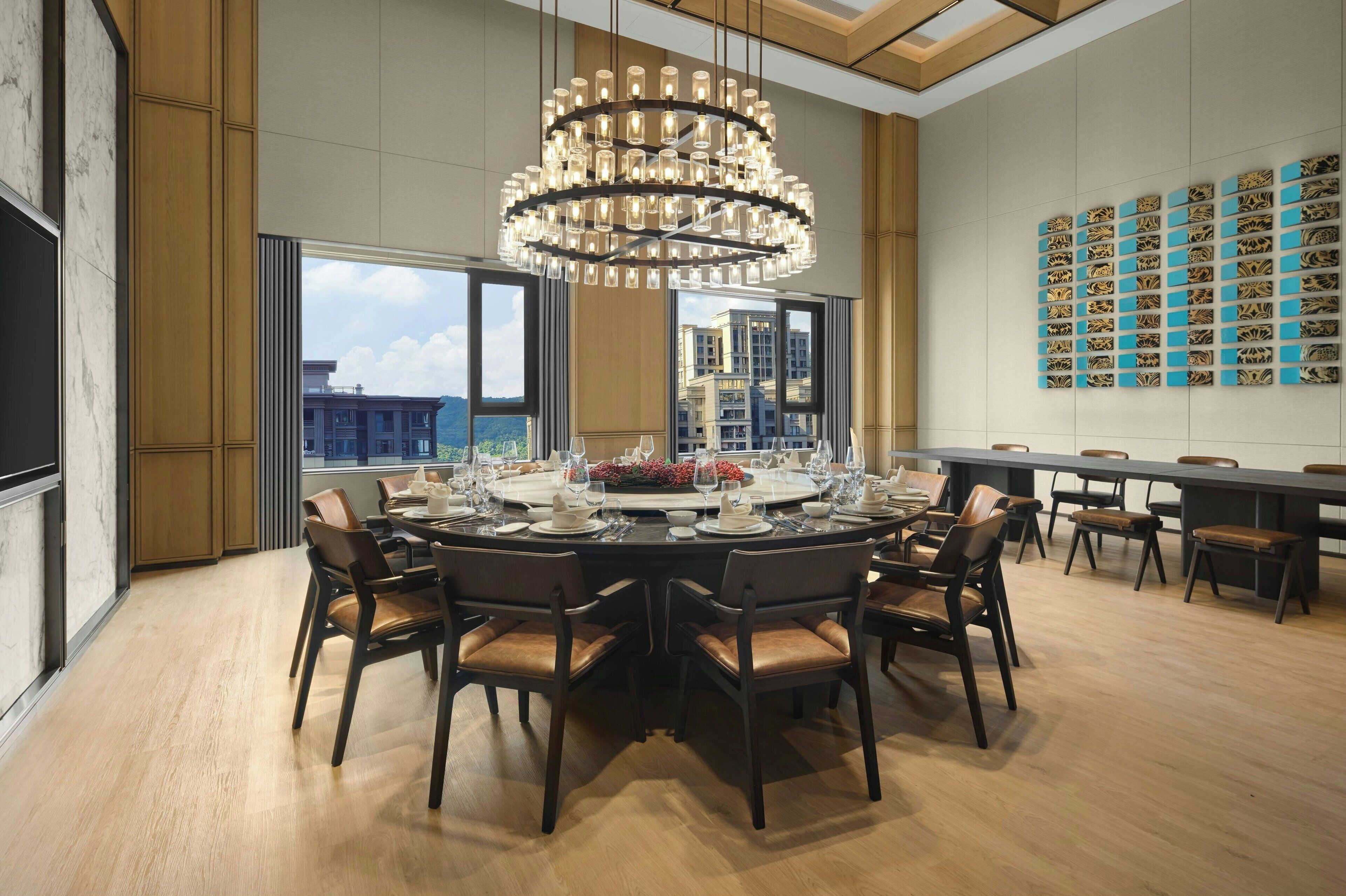 A modern dining area with a large chandelier, round dining table, and multiple chairs.