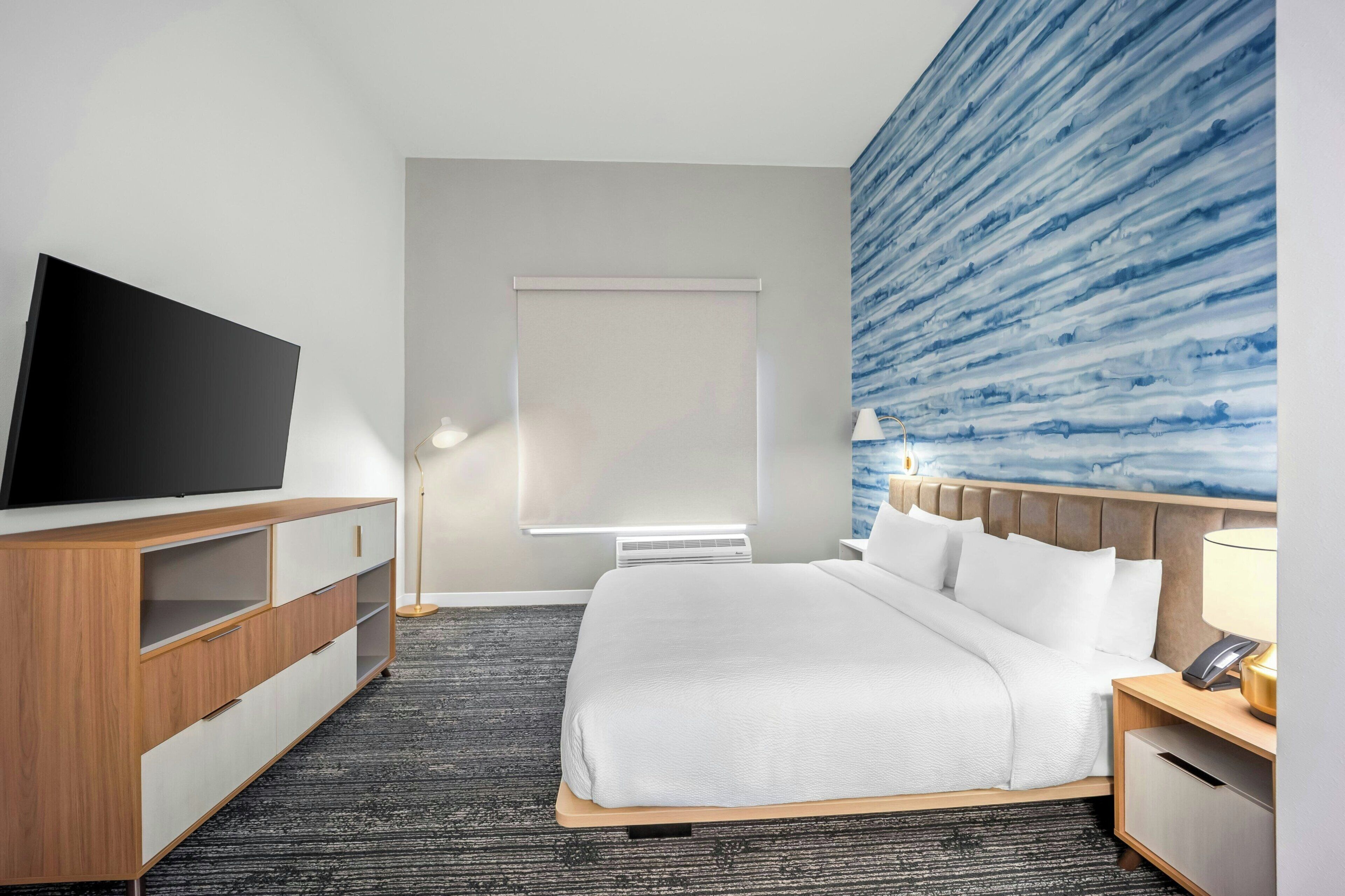 Habitación de hotel con cama, televisión, escritorio y pared con un diseño abstracto azul.