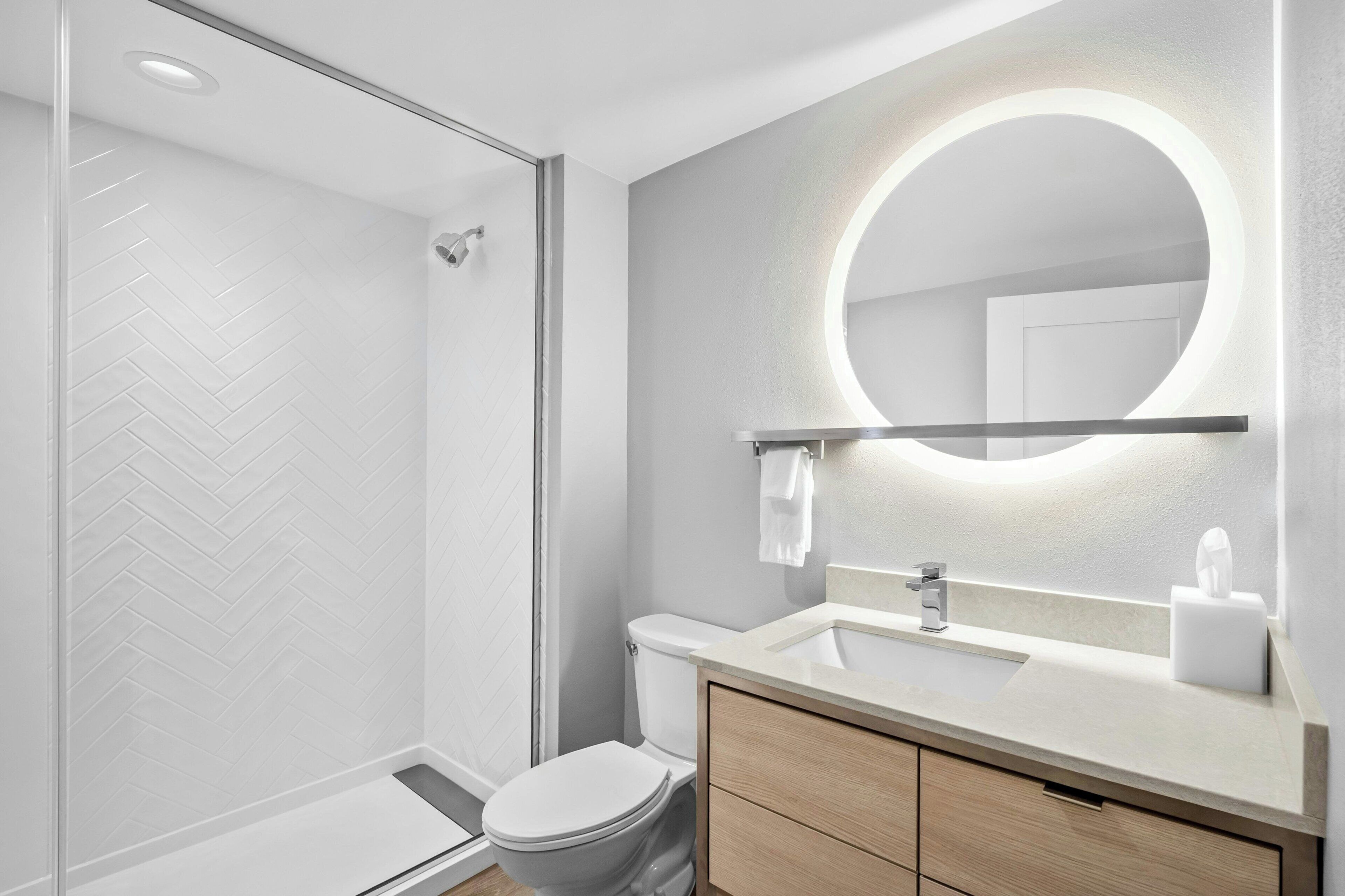 Une salle de bain moderne avec une douche à parois de verre, des toilettes, un lavabo avec un miroir et un porte-serviettes.