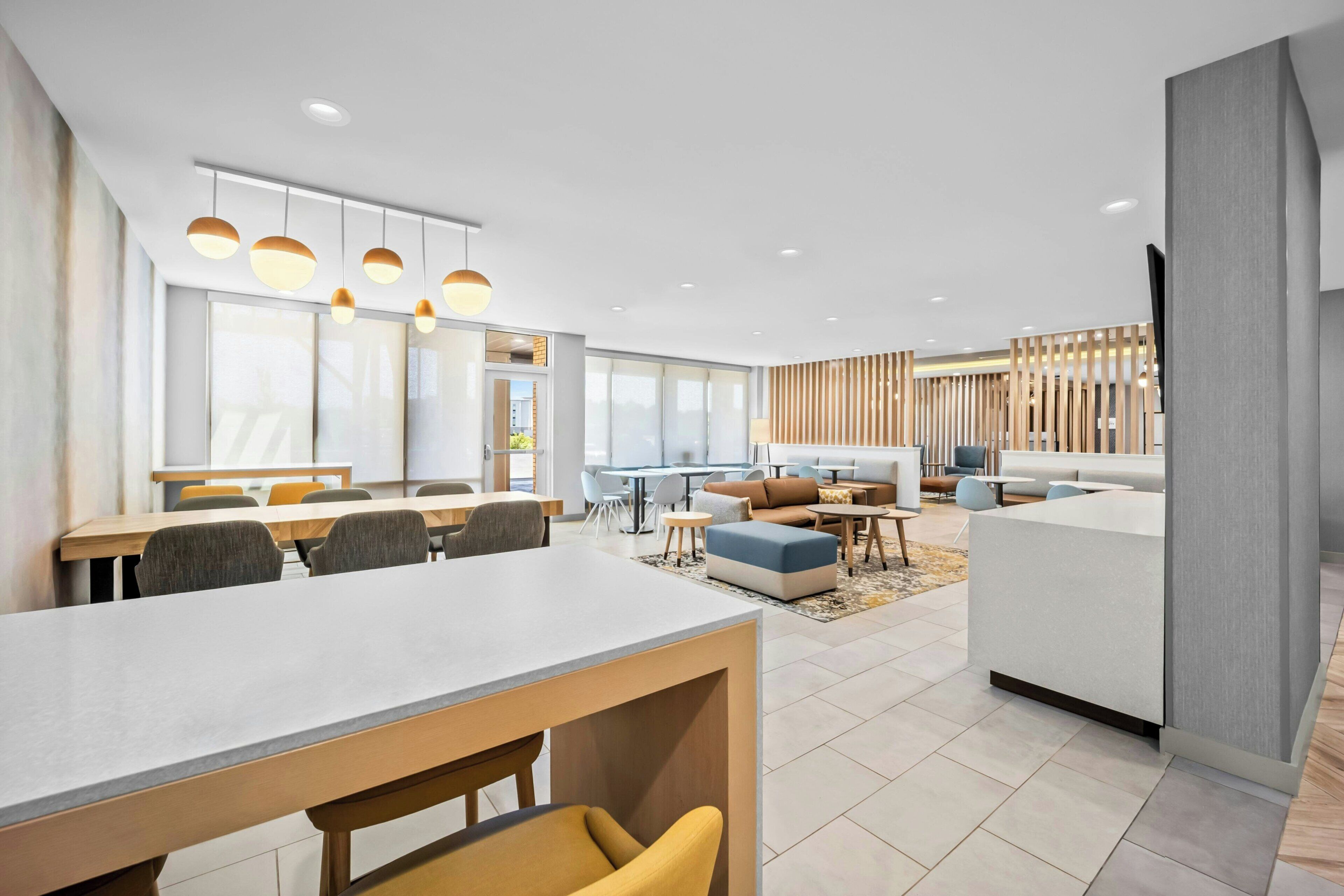 A modern hotel lobby with a dining area, seating, and a reception desk.