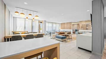 A modern hotel lobby with a dining area, seating, and a reception desk.