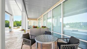 A modern outdoor seating area with a round table and wicker chairs, large windows, and potted plants.