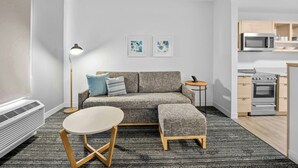 A modern living room with a sofa, a small round table, a floor lamp, and a kitchen area with a microwave and oven.