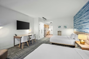 A hotel room with a bed, a desk with a chair, a television, and a painting on the wall.
