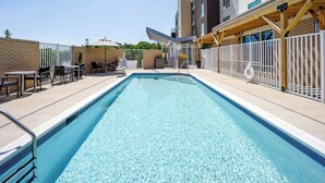 A rectangular swimming pool with a tiled edge, surrounded by a white fence, and adjacent to a building with a brick facade and windows. - Towneplace Suites by Marriott Kernersville (Kernersville)
