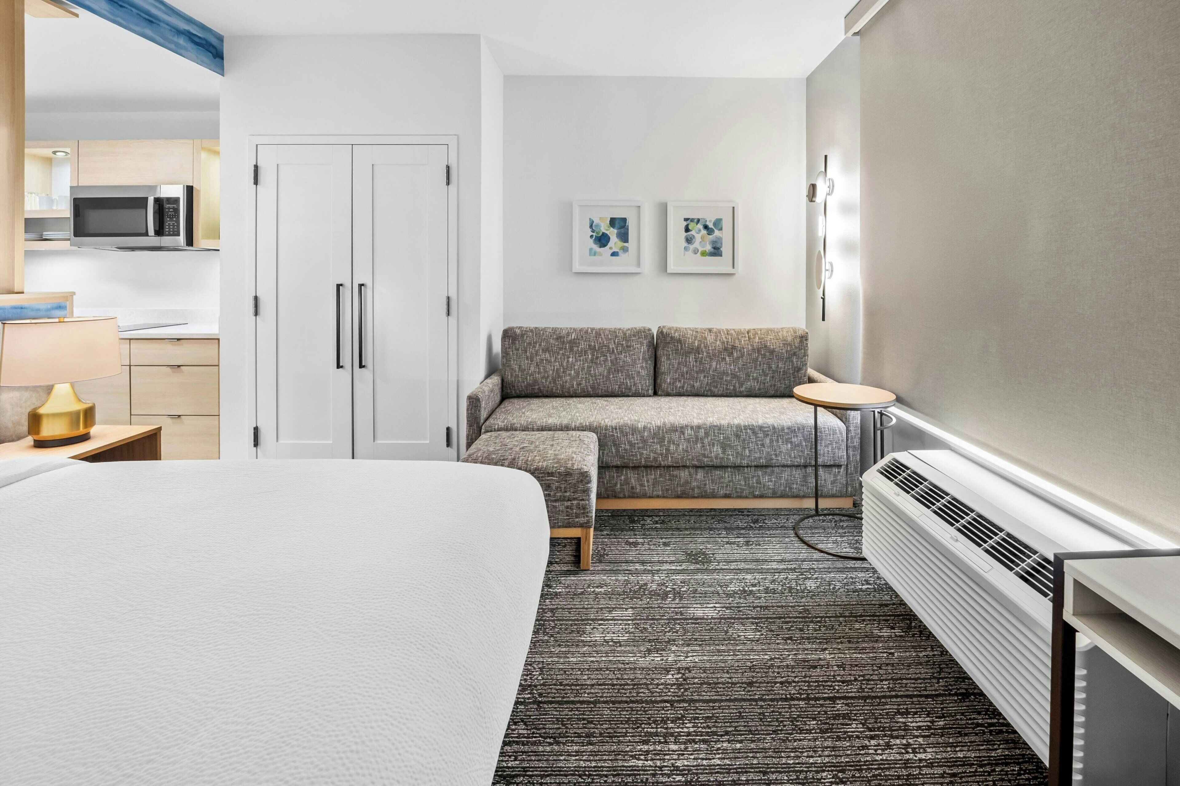 A hotel room with a bed, a sofa, a small table, a microwave, and a heater.