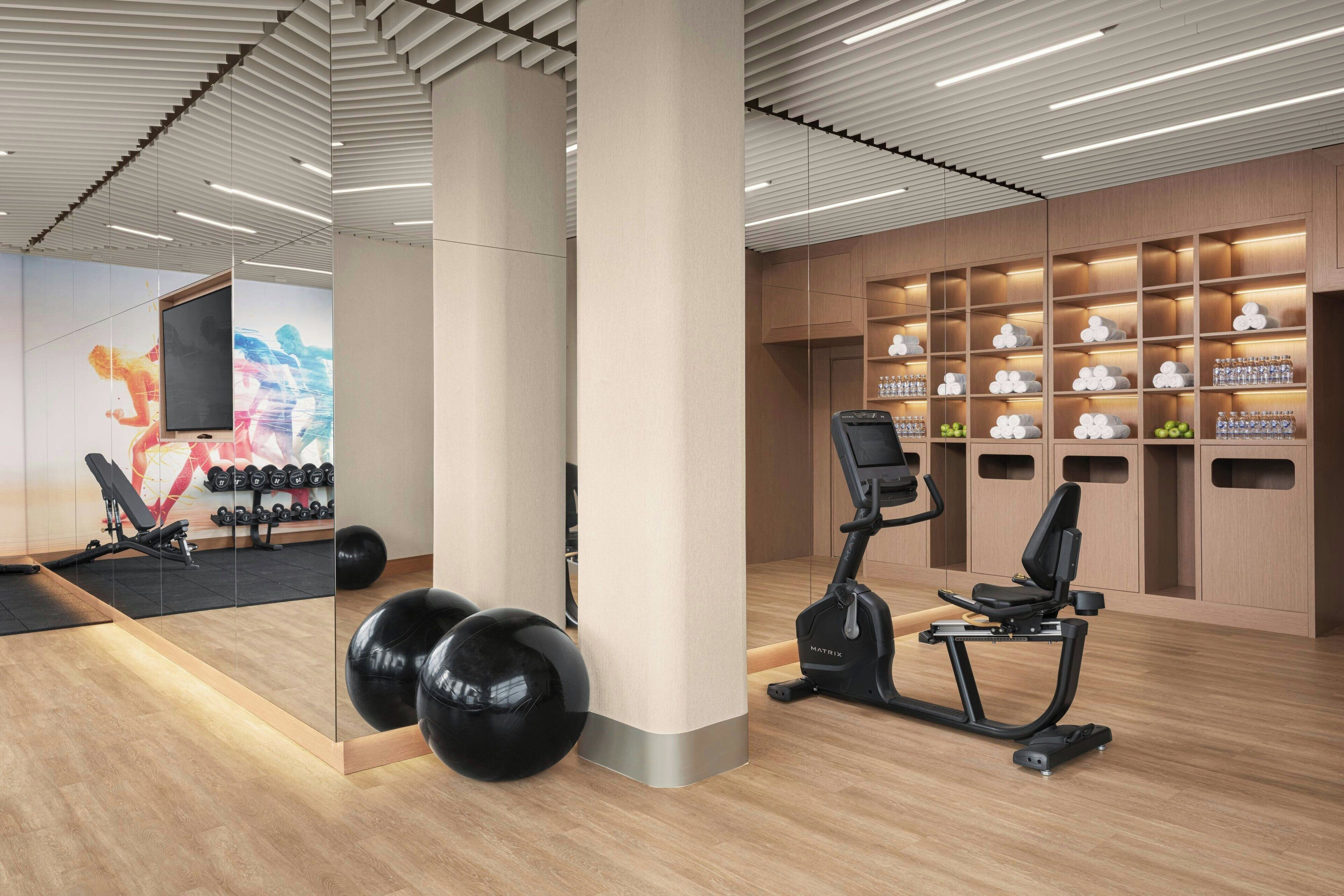 Ein modernes Fitnessstudio mit Trainingsgeräten, einer Spiegelwand und einer Wand mit ordentlich angeordneten Flaschen und Gläsern.