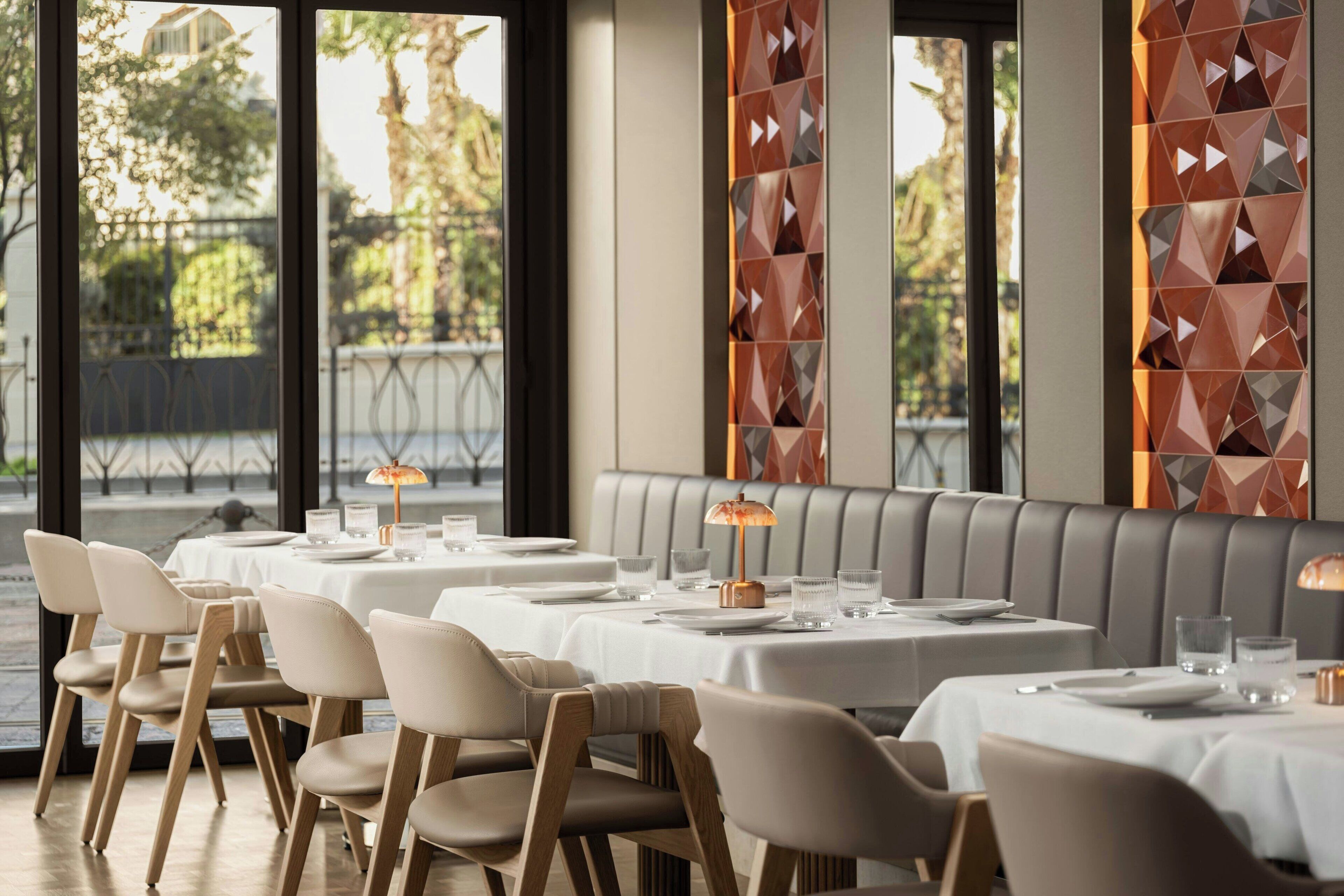 A restaurant with tables set for dining, a view of the outdoors, and a modern interior design.