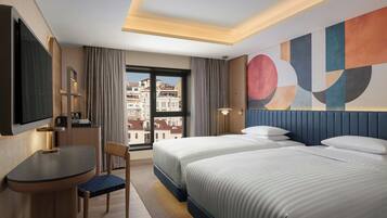 Ein Hotelzimmer mit Bett, Schreibtisch, Stuhl, Fernseher und Blick auf Gebäude.