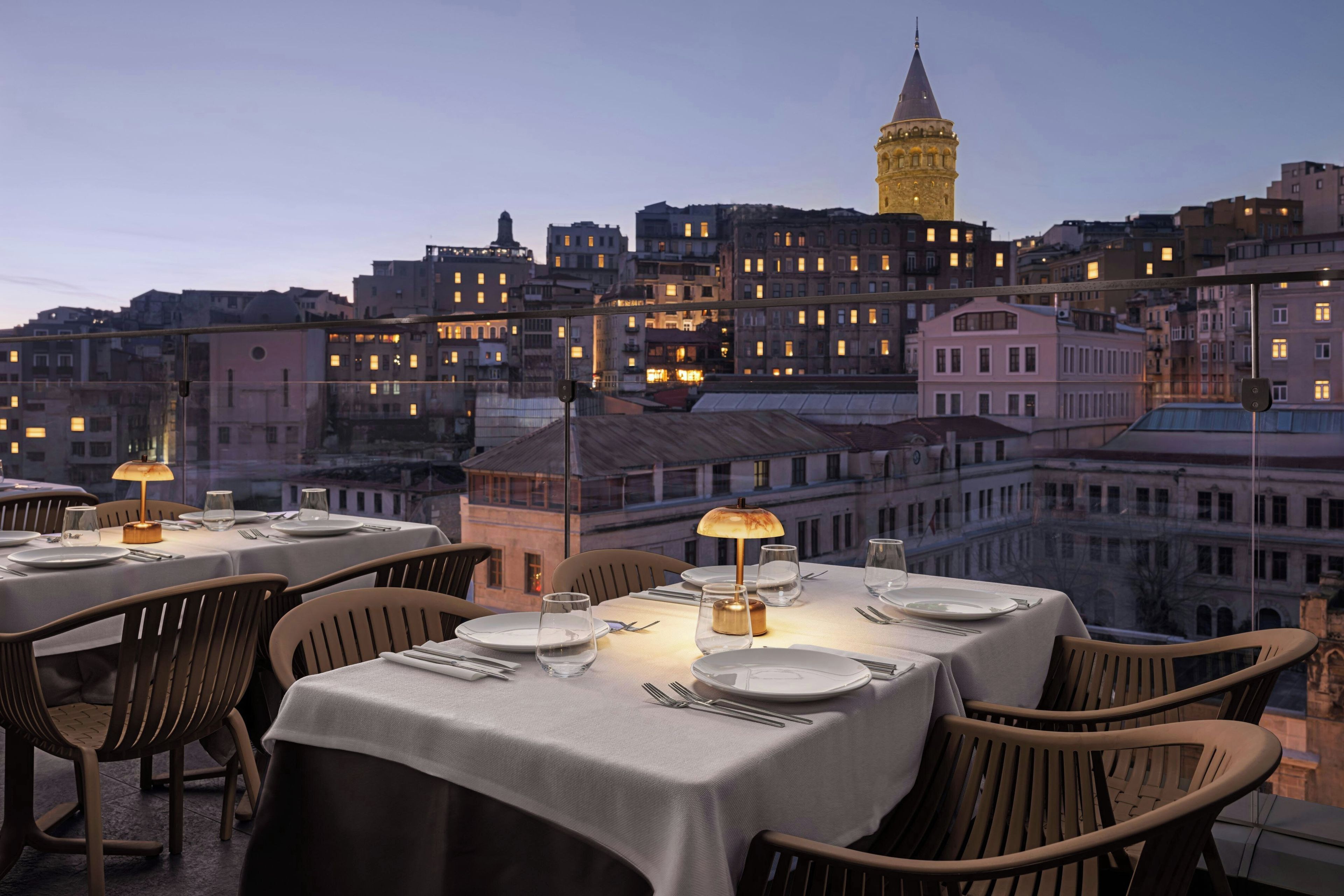 A rooftop dining area with tables set for two, overlooking a cityscape with historic buildings and a prominent tower.