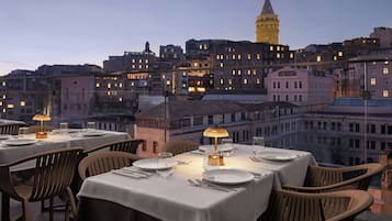 A rooftop dining area with tables set for two, overlooking a cityscape with historic buildings and a prominent tower.