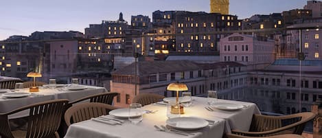 A rooftop dining area with tables set for two, overlooking a cityscape with historic buildings and a prominent tower.