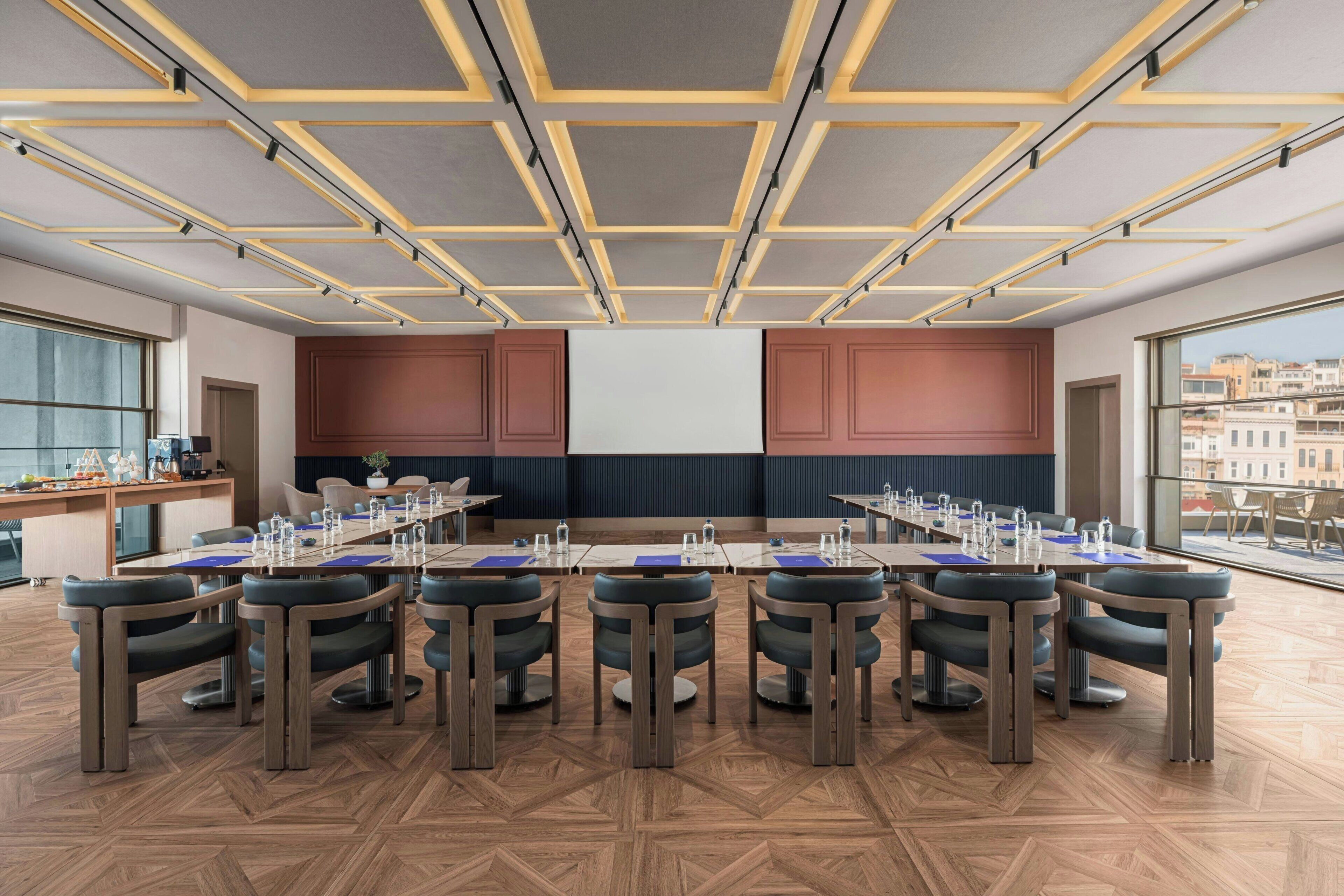 Une salle de conférence avec une longue table, des chaises et une vue sur les bâtiments, grâce à de grandes fenêtres.