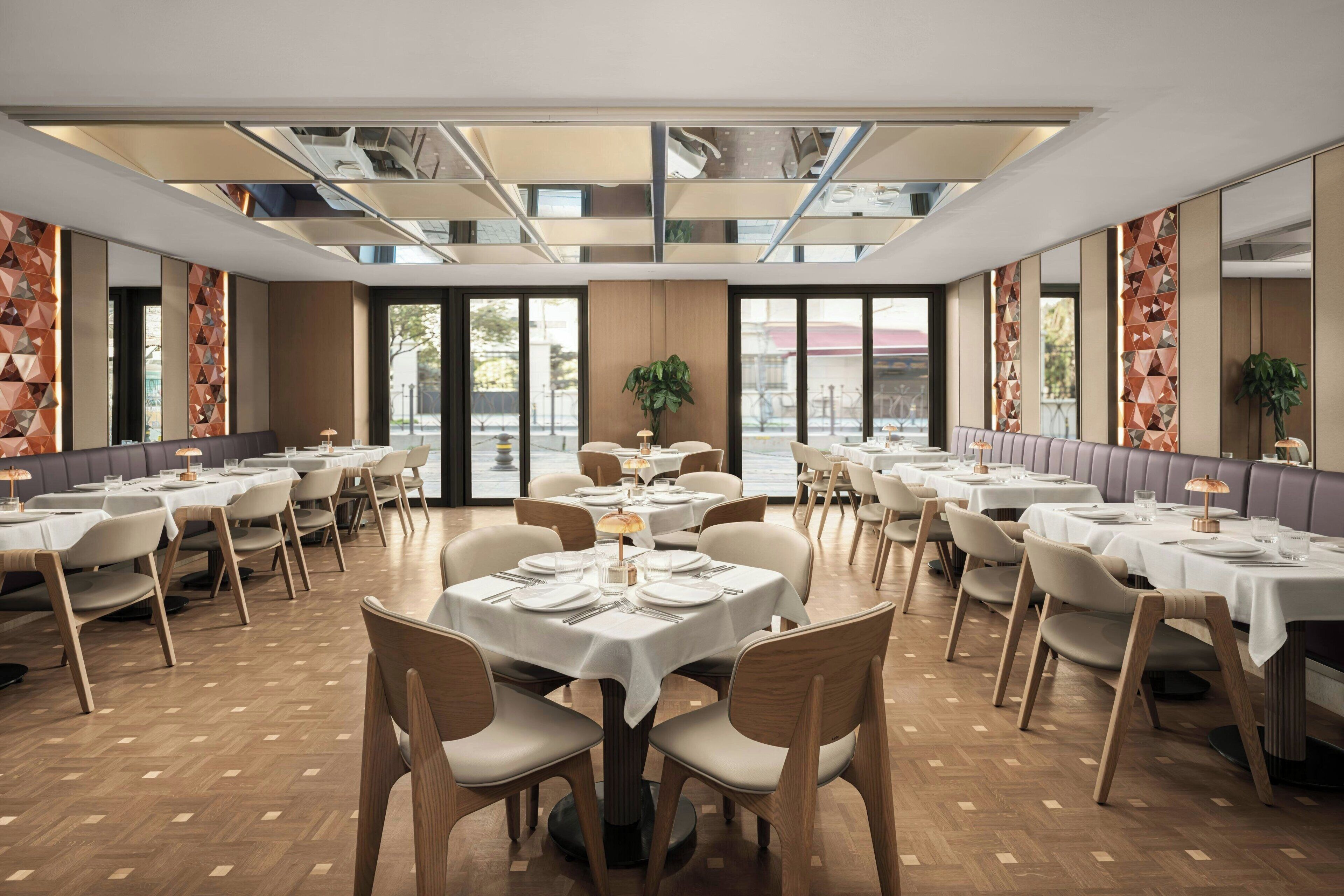 A spacious dining area with multiple tables and chairs, large windows, and a modern ceiling design.