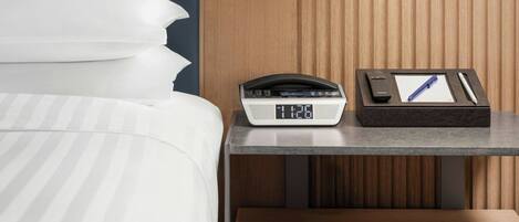 A hotel room with a bed, bedside table, lamp, and a clock.