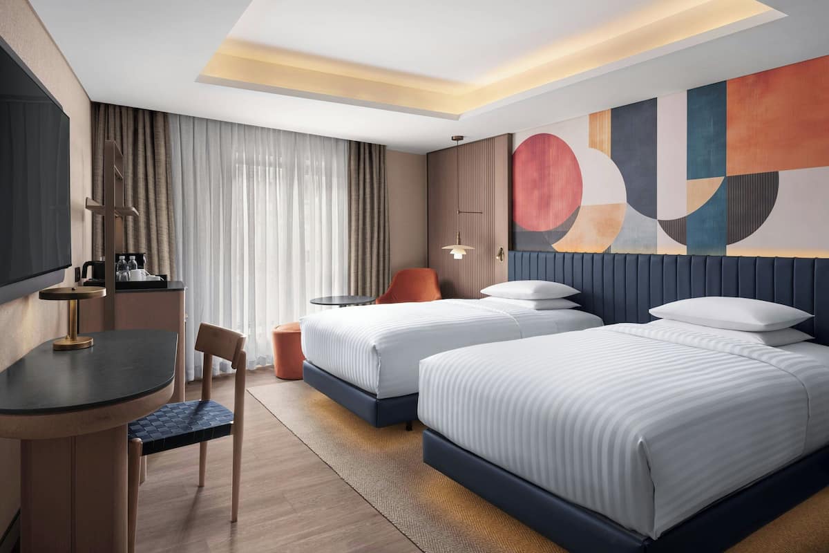 A modern hotel room with two beds, a desk, and a seating area.