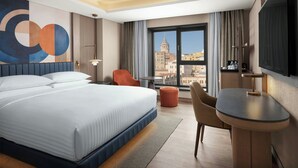 A hotel room with a large bed, a desk, a chair, a TV, and a view of a cityscape. - Delta Hotels by Marriott Istanbul Karakoy (Istanbul)