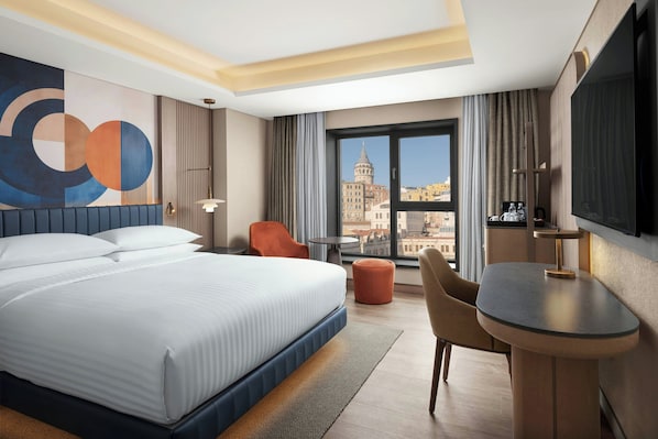 A hotel room with a large bed, a desk, a chair, a TV, and a view of a cityscape. - Delta Hotels by Marriott Istanbul Karakoy (Istanbul)