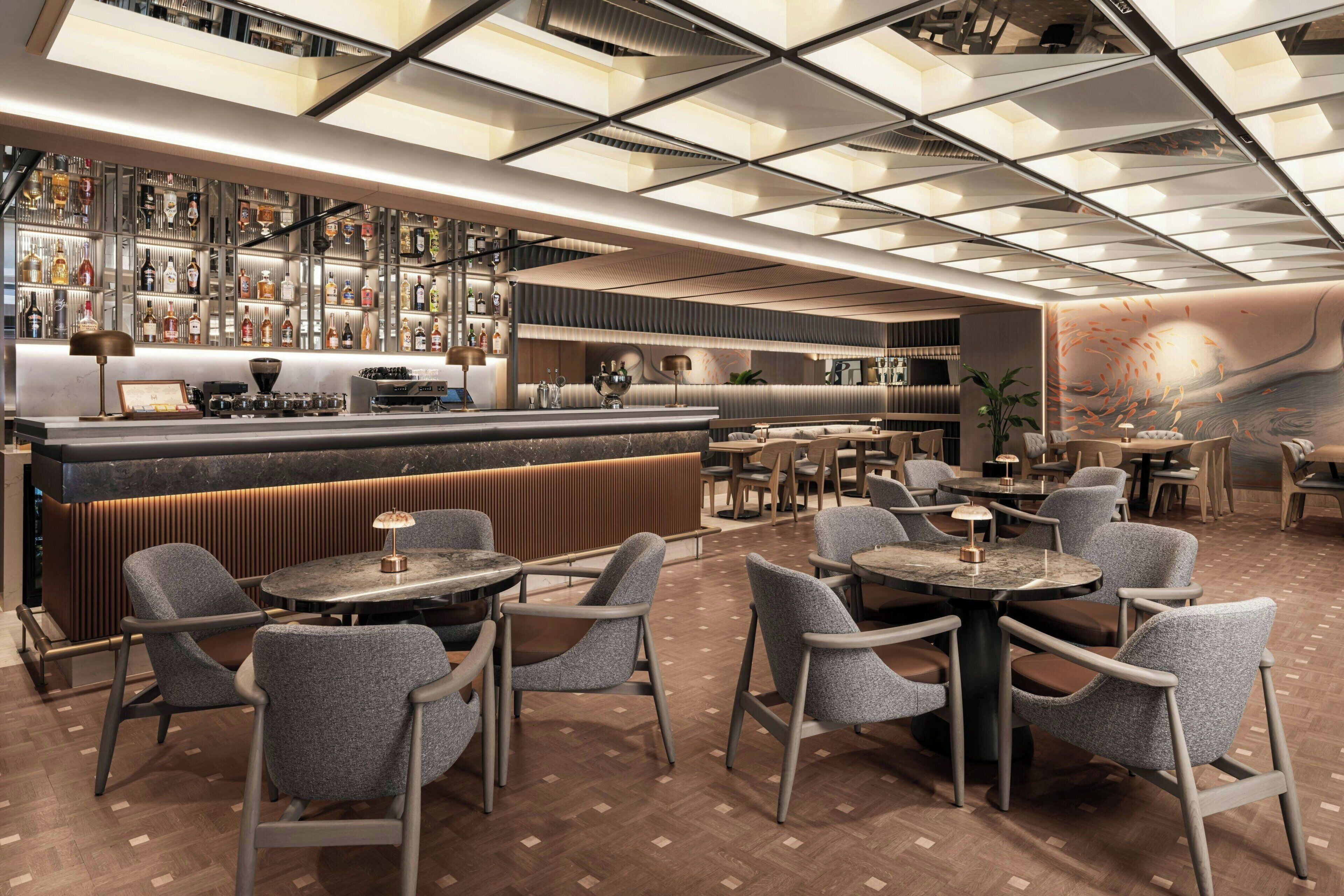 A modern bar area with a long counter, multiple seating options, and a patterned ceiling.