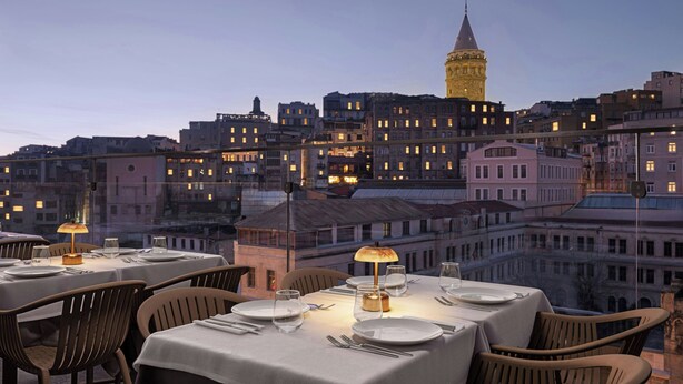 A dining area with tables set for two, overlooking a cityscape with historic buildings and a prominent tower. - Delta Hotels by Marriott Istanbul Karakoy (Istanbul)
